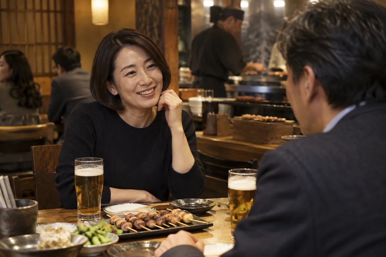 焼き鳥屋で、ビールと料理を前に会話を楽しむ40代半ばの女性と男性。