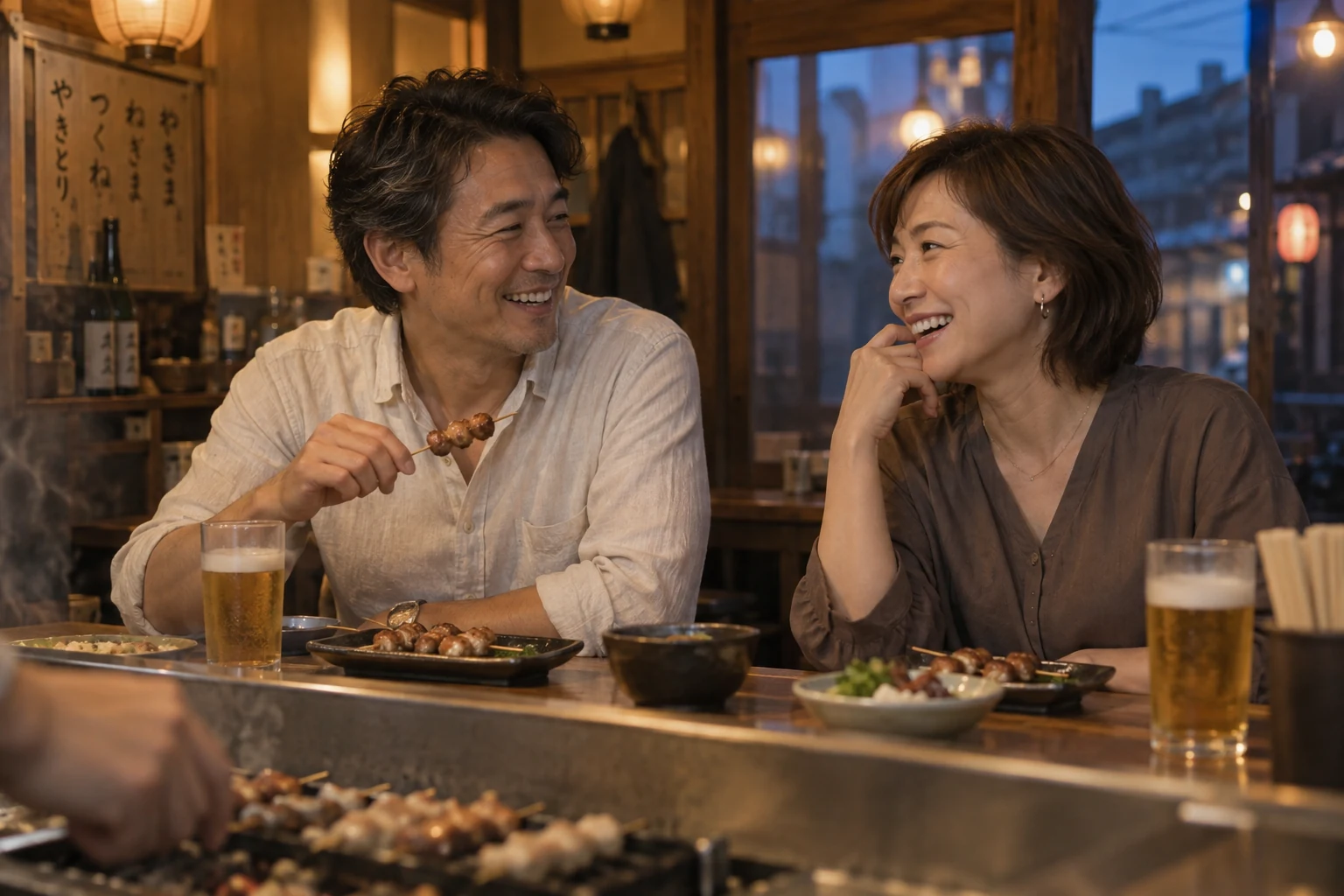 夕暮れの焼き鳥屋で、焼き鳥とビールを前に笑い合う40代半ばの男女。